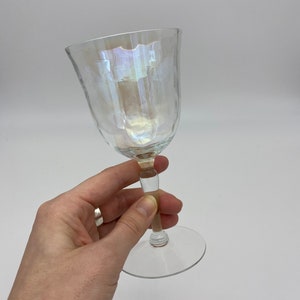 K&ouml;nnte beinhalten: Ein klares, schillerndes Weinglas mit strukturierter Oberfl&auml;che. Das Glas hat eine abgerundete Schale und einen schlanken Stiel. Der Fu&szlig; ist flach und kreisf&ouml;rmig. Das Glas wird vor einem wei&szlig;en Hintergrund gehalten.