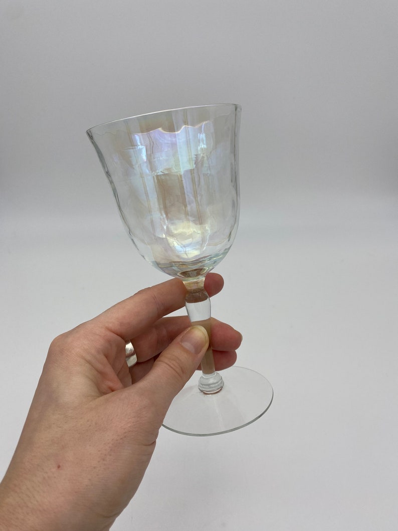 K&ouml;nnte beinhalten: Ein klares, schillerndes Weinglas mit strukturierter Oberfl&auml;che. Das Glas hat eine abgerundete Schale und einen schlanken Stiel. Der Fu&szlig; ist flach und kreisf&ouml;rmig. Das Glas wird vor einem wei&szlig;en Hintergrund gehalten.