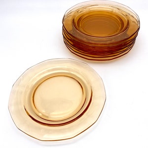 Puede incluir: Una pila de platos de postre de vidrio &aacute;mbar con un borde festoneado. Los platos est&aacute;n apilados sobre una superficie blanca.