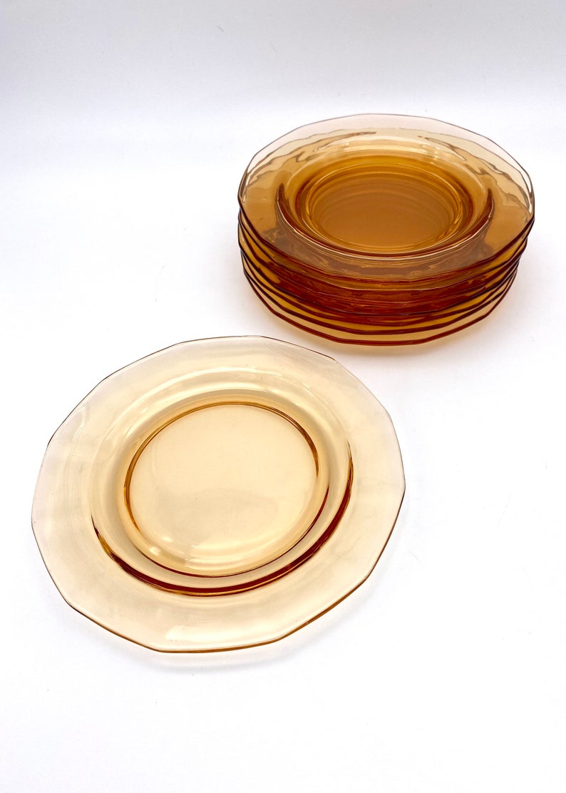 Puede incluir: Una pila de platos de postre de vidrio &aacute;mbar con un borde festoneado. Los platos est&aacute;n apilados sobre una superficie blanca.