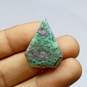 May include: A faceted gemstone with a green and pink mottled pattern. The stone has a geometric shape with a pointed top and a multi-sided base. The colours are a mix of green and pink, with a textured appearance.