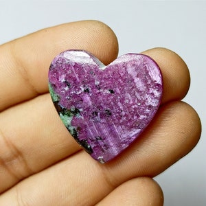 Könnte beinhalten: Ein herzförmiger Edelstein in leuchtendem Magenta mit schwarzen und grünen Streifen. Die Oberfläche des Steins weist ein strukturiertes, natürliches Muster auf. Ideal für die Schmuckherstellung. Abmessungen ca. 3 cm.