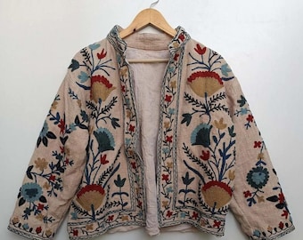 以下が含まれることがあります： 青、赤、茶色の花柄が刺繍されたベージュのジャケット。ジャケットはフロントジッパー留め、襟付きです。