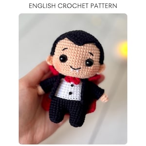 May include: A handmade crochet doll of a vampire, wearing a black suit, red bow tie, and cape. The doll has a smiling face, black hair, and large black eyes. The text "ENGLISH CROCHET PATTERN" is at the top.
