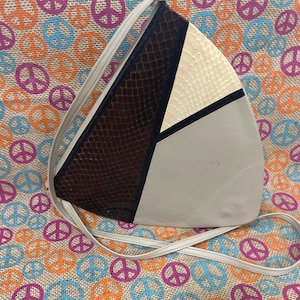 May include: A triangular handbag with a geometric design. The bag features sections of brown snakeskin, off-white, and light grey. A thin, white strap extends from the top corners. The bag is set against a colourful background with peace symbols.
