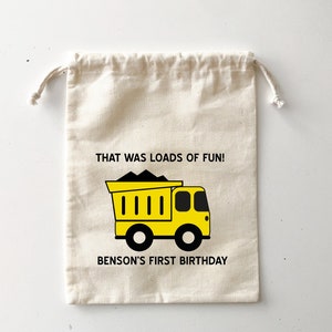 Könnte beinhalten: Ein weißer Baumwollbeutel mit Kordelzug, bedruckt mit einem gelben Kipplaster und dem Text "That was loads of fun! Benson's First Birthday".