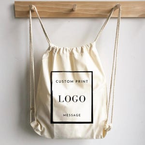 May include: A white drawstring bag with black text that says "CUSTOM PRINT", "LOGO", and "MESSAGE".