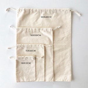 May include: Four off-white drawstring bags made of fabric, arranged by size from smallest to largest. The bags are labeled with the dimensions 10x13cm, 15x20cm, 20x30cm, and 30x40cm. Each bag features a simple pull-string closure at the top opening.
