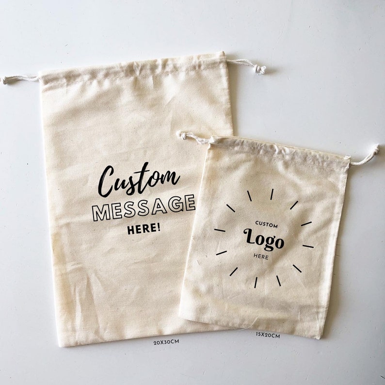 May include: Two off-white cotton drawstring bags with black text. The larger bag, labeled 20x30cm, features the text Custom MESSAGE HERE!. The smaller bag, labeled 15x20cm, features the text CUSTOM Logo HERE surrounded by a circular line design.