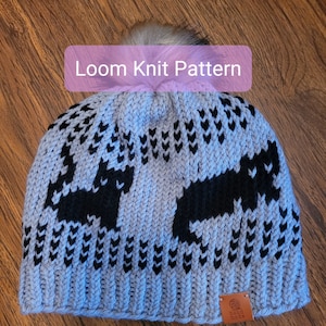 May include: A blue and black knit hat with a pom pom on top. The hat has a pattern of black hearts and arrows. The hat has a brown leather tag that says "hand made".
