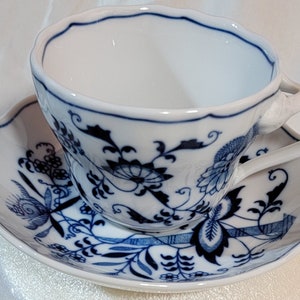May include: A white porcelain teacup and saucer with a blue and white floral pattern. The cup has a scalloped rim and a handle. The saucer has a scalloped edge.