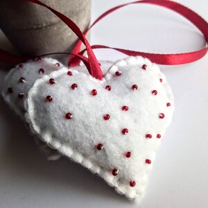 May include: Two white felt hearts with red bead accents, attached to a red ribbon.