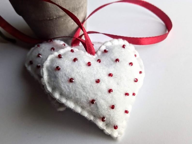 May include: Two white felt hearts with red bead accents, attached to a red ribbon.