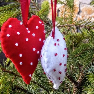 May include: Two felt heart ornaments, one red with white polka dots and one white with red polka dots, hanging from a Christmas tree.