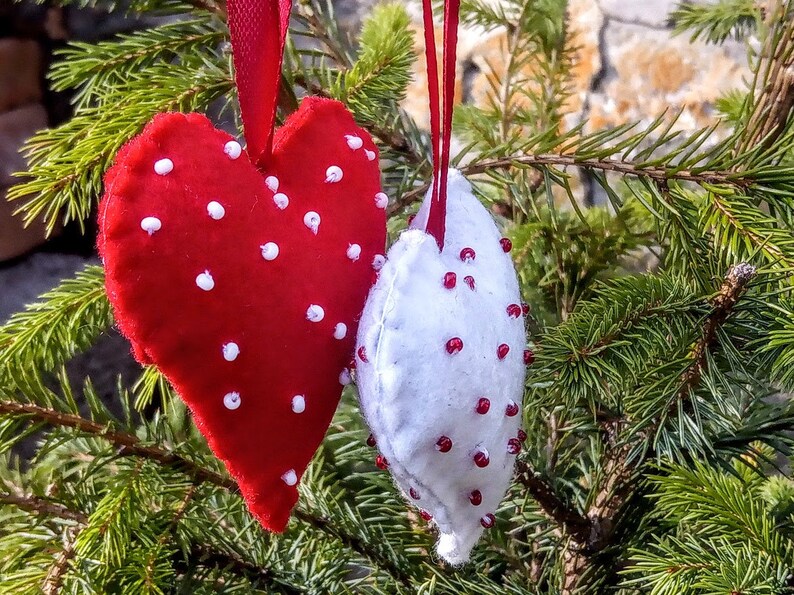 May include: Two felt heart ornaments, one red with white polka dots and one white with red polka dots, hanging from a Christmas tree.