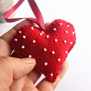 May include: A red felt heart with white polka dots, hanging from a red ribbon. The heart is handmade and has a soft, plush texture.