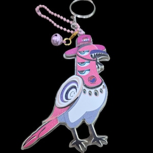 May include: A pink and white bird-shaped keychain with a hat and multiple eyes. The keychain has a silver ring and a pink beaded chain with a small, round charm. The bird has a unique design with a mix of colors and patterns.