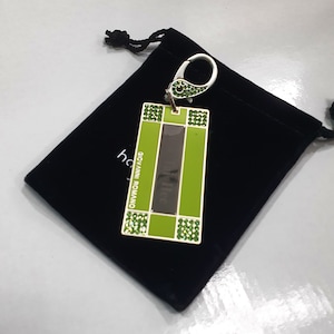 May include: A green and silver keychain with a black background. The keychain has a silver ring and a green rectangular charm with the text "GIOVANNI ROMANO" and green rhinestones.