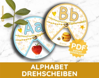 Può includere: Due ruote di apprendimento dell'alfabeto colorate con un motivo a stelle e cuori. La prima ruota ha la lettera "A" e una mela. La seconda ruota ha la lettera "B" e un alveare con un'ape. Il testo "Alphabet Drehscheiben" è nella parte inferiore dell'immagine.