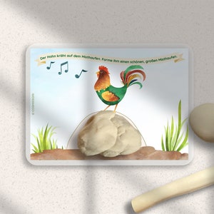 May include: A colorful illustration of a rooster crowing on a pile of dirt. The text on the card reads "Der Hahn kr&uuml;ht auf dem Misthaufen.  Forme ihm einen sch&ouml;nen, gro&szlig;en Misthaufen."