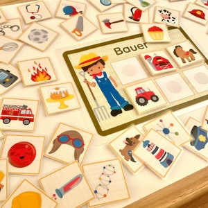Puede incluir: Un conjunto colorido de tarjetas de juego de memoria con varias im&aacute;genes, incluyendo un granjero, un cami&oacute;n de bomberos, un faro, un granero y un tractor. El tablero de juego tiene la palabra "Bauer" impresa, que es alem&aacute;n para "granjero".