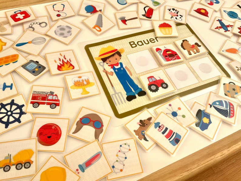 Puede incluir: Un conjunto colorido de tarjetas de juego de memoria con varias im&aacute;genes, incluyendo un granjero, un cami&oacute;n de bomberos, un faro, un granero y un tractor. El tablero de juego tiene la palabra "Bauer" impresa, que es alem&aacute;n para "granjero".