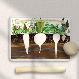 May include: A white card with a colorful illustration of a garden with three empty spaces for play dough. The text on the card reads "Im Gemuesegarten ist bald Erntezeit.  Forme grosse Rueben!"
