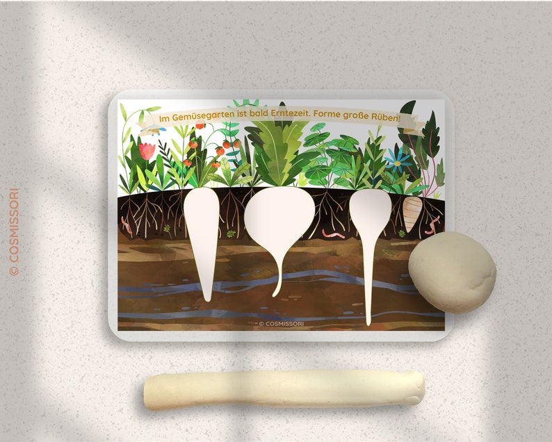 May include: A white card with a colorful illustration of a garden with three empty spaces for play dough. The text on the card reads "Im Gemuesegarten ist bald Erntezeit.  Forme grosse Rueben!"
