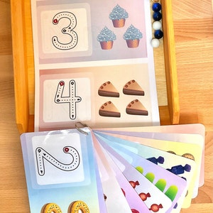 May include: A set of colourful flashcards with numbers 1 through 4, each featuring a different image. The numbers are outlined in black with red dots for starting points. The images include cupcakes, cake slices, doughnuts, and sweets. The text "http://cosmissorletsy.com" is printed at the top of the cards.
