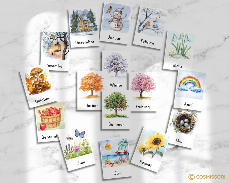 May include: A set of 12 illustrated cards depicting the months of the year with corresponding seasonal imagery. The cards feature watercolor illustrations of a snowman, a robin, a house, snowdrops, a rainbow, a bird's nest, a sunflower, a beach scene, a butterfly, mushrooms, apples in a basket, and a tree with fall leaves. Each card has the name of the month written below the image in German.