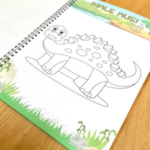 May include: A black and white line drawing of a dinosaur on a white page with a green border. The dinosaur is facing the right side of the page. The text "MALE AUS!" is visible in the upper right corner of the page.