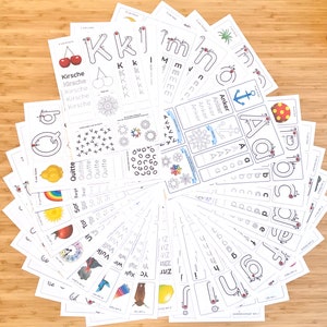 May include: A set of 26 alphabet flashcards with tracing lines and German words for each letter. The flashcards are printed on white paper and feature colorful illustrations.