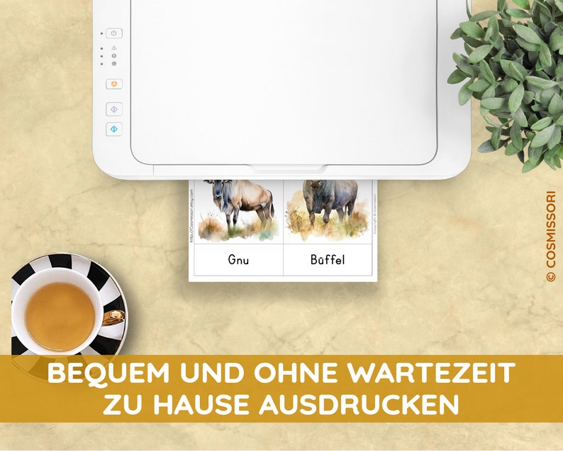 May include: A white printer printing animal flashcards with watercolor illustrations of a gnu and a buffalo. The flashcards have the words "Gnu" and "B&uuml;ffel" printed on them. A cup of tea in a black and white striped cup and saucer is in the lower left corner.