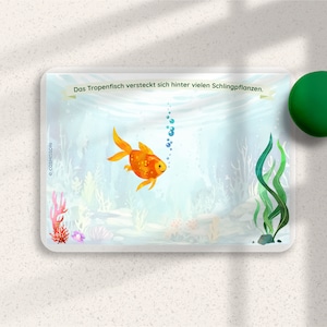 May include: A colorful illustration of a goldfish swimming in an underwater scene with green seaweed and bubbles. The text "Das Tropenfisch versteckt sich hinter vielen Schlingpflanzen." is at the top of the image.