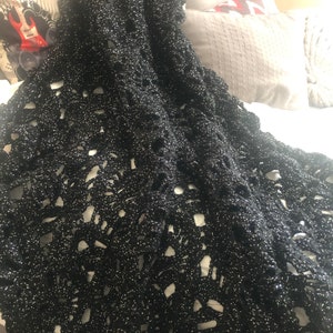 May include: Black crochet throw blanket with a sparkly finish. The blanket has a delicate openwork pattern.