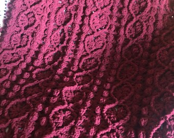 May include: A burgundy crocheted throw blanket with a textured, floral pattern.