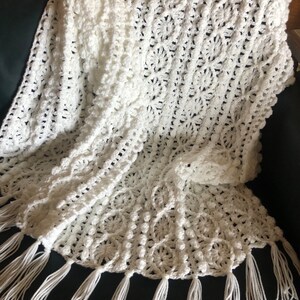 May include: White crochet throw blanket with a delicate floral pattern and fringe trim.