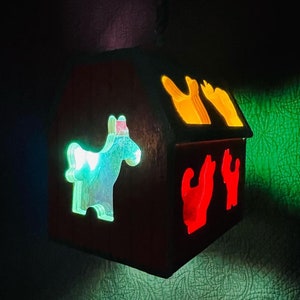 May include: A wooden barn-shaped nightlight with a green horse, red cats, and yellow birds cutouts. The light shines through the cutouts, creating a colorful glow.