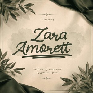 以下が含まれることがあります： ベージュ色の背景に、手書き風のダークグリーンのフォントで「Zara Amorett」と書かれています。ダークグリーンの線で下線が引かれています。「Handwriting Script Font by Letterhanna Studio」というテキストが下にあります。装飾的な葉と濃い緑色の布がテキストを囲んでいます。
