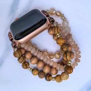 May include: A rose gold Apple Watch with a brown and beige beaded band. The band is made of multiple strands of beads, including wood, stone, and glass.