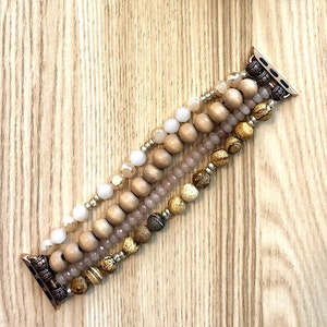 May include: A multi-strand beaded Apple Watch band with brown, beige, and white beads. The band is made of wood, glass, and stone beads.