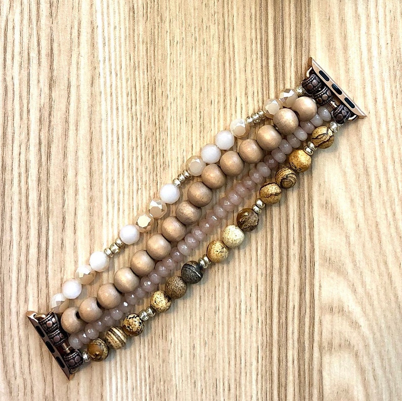 May include: A multi-strand beaded Apple Watch band with brown, beige, and white beads. The band is made of wood, glass, and stone beads.