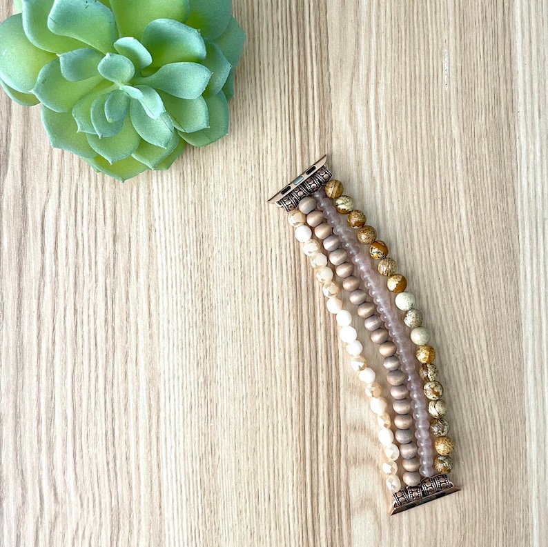 May include: A multi-strand beaded Apple Watch band with a mix of beige, brown, and gold beads. The band is made of natural stones and has a metal clasp.