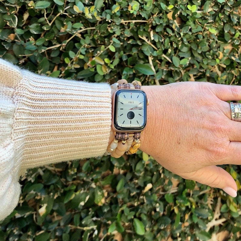 May include: A rose gold Apple Watch with a brown and white beaded band. The watch face displays the date "FRI 5".