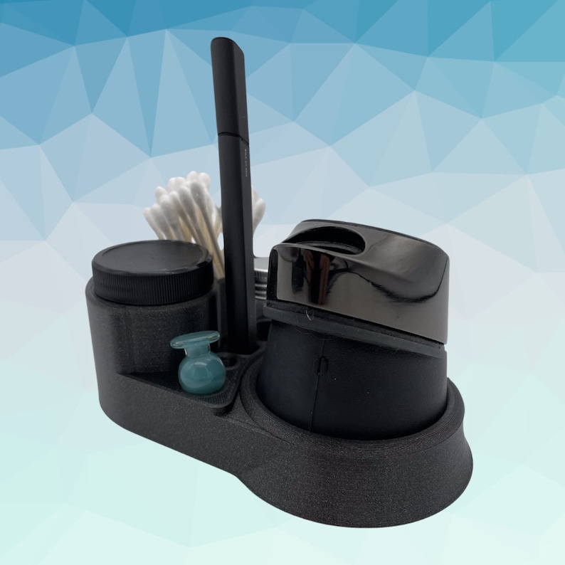 K&ouml;nnte beinhalten: Ein schwarzer Plastik-Organizer mit F&auml;chern f&uuml;r verschiedene Gegenst&auml;nde. Er enth&auml;lt ein kleines Glas, einen runden Beh&auml;lter mit schwarzem Deckel, einen kleinen blauen Beh&auml;lter und einen schwarzen Stifthalter. Au&szlig;erdem befinden sich Wattest&auml;bchen im Stifthalter.
