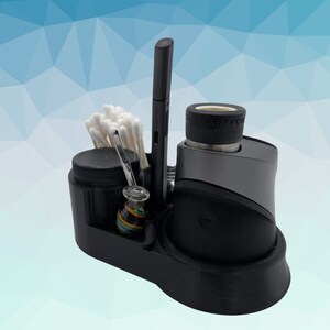 K&ouml;nnte beinhalten: Ein schwarzer und grauer 3D-gedruckter Organizer mit einem Fach f&uuml;r einen Vape-Stift, ein kleines Glas, eine Glaspfeife und Wattest&auml;bchen. Der Organizer hat eine schwarze Basis und eine graue Oberseite mit einem runden Knopf.