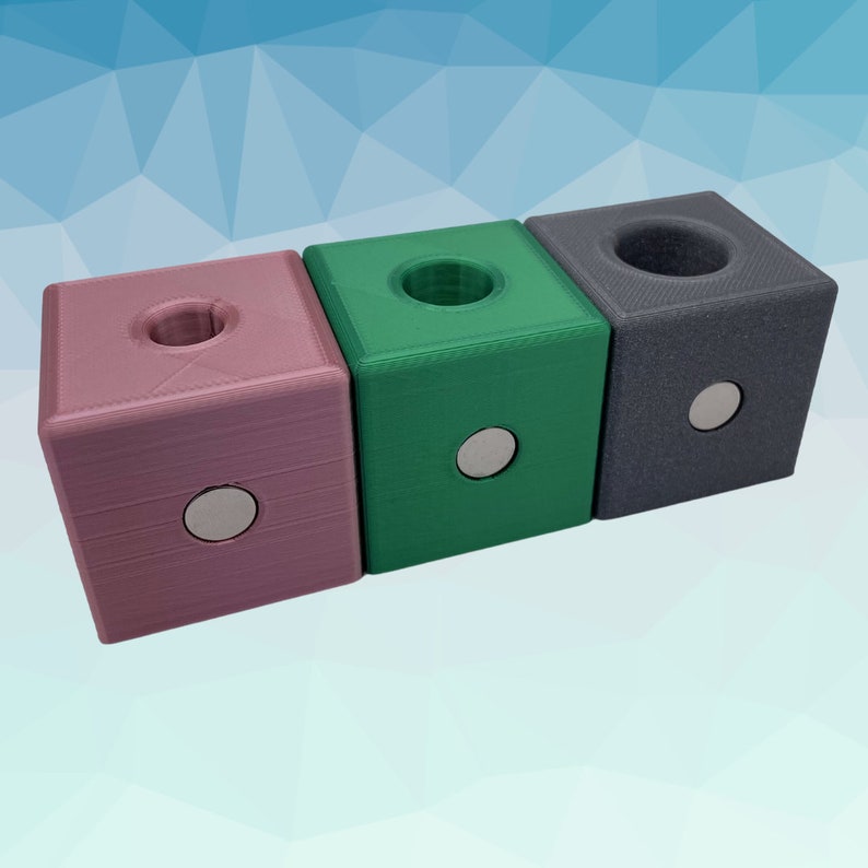 Puede incluir: Tres peque&ntilde;as cajas cuadradas con un agujero redondo en la parte superior. Las cajas son de color rosa, verde y gris.