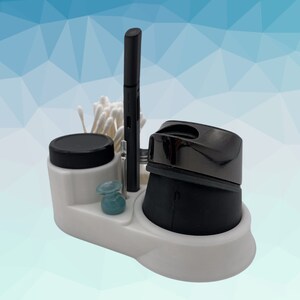 K&ouml;nnte beinhalten: Wei&szlig;er Organizer mit einem schwarzen Stift, einem kleinen Glas, einem schwarzen und silbernen Elektrorasierer und Wattest&auml;bchen.