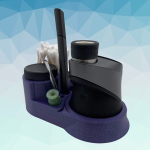 K&ouml;nnte beinhalten: Ein lila Organizer mit F&auml;chern f&uuml;r einen Vape-Stift, ein kleines Glas, ein Werkzeug und Wattest&auml;bchen. Der Vape-Stift ist schwarz und hat eine silberne Basis mit dem Wort "PUFFCO" darauf.