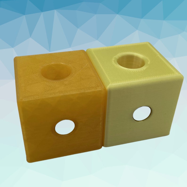 Puede incluir: Dos cubos impresos en 3D, uno amarillo y otro naranja, con un agujero en la parte superior y un agujero m&aacute;s peque&ntilde;o en el lateral.
